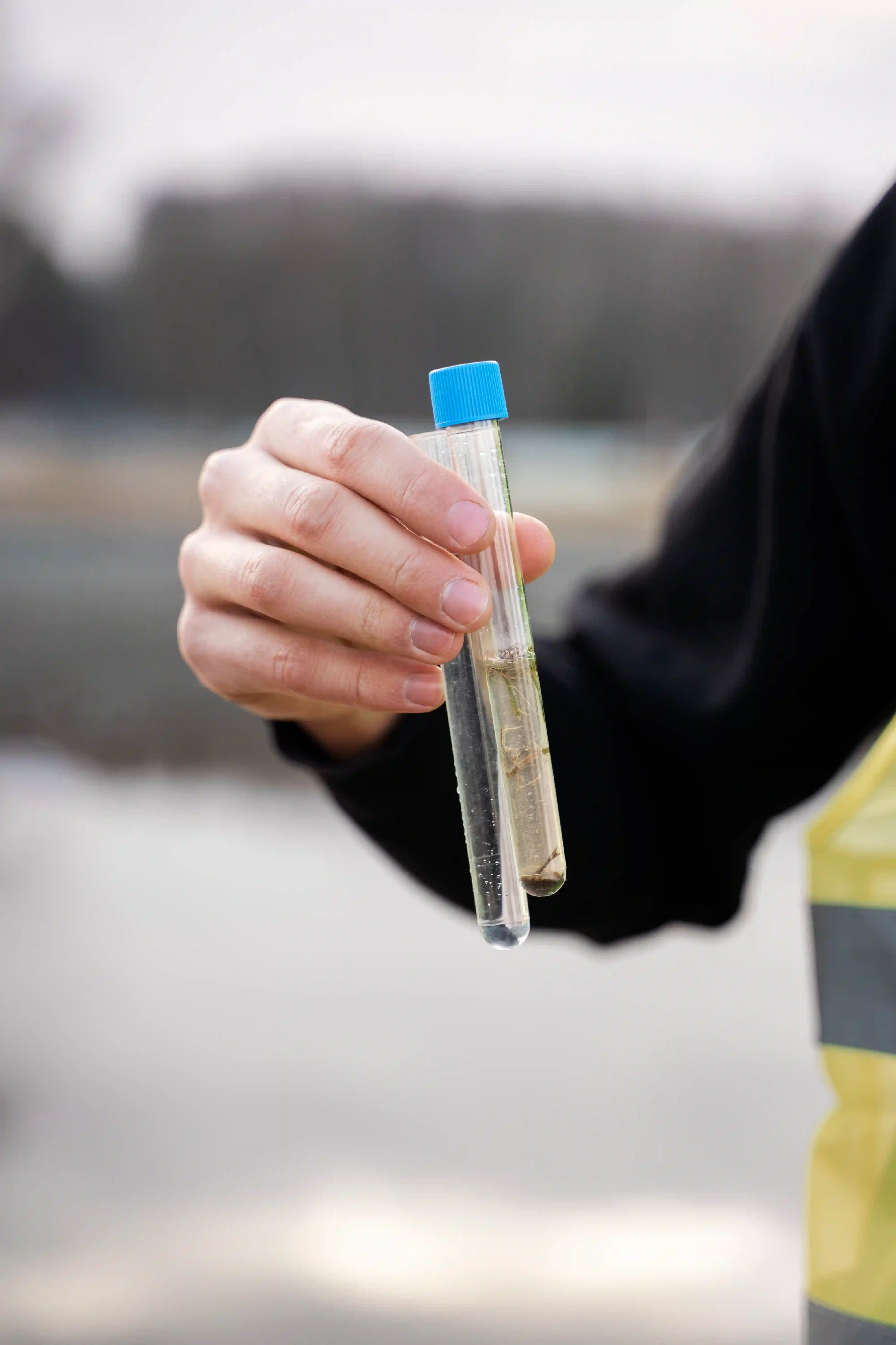 Mano de un técnico sujetando tubos de ensayo con muestras de agua para análisis de pureza y detección de microorganismos en un depósito.