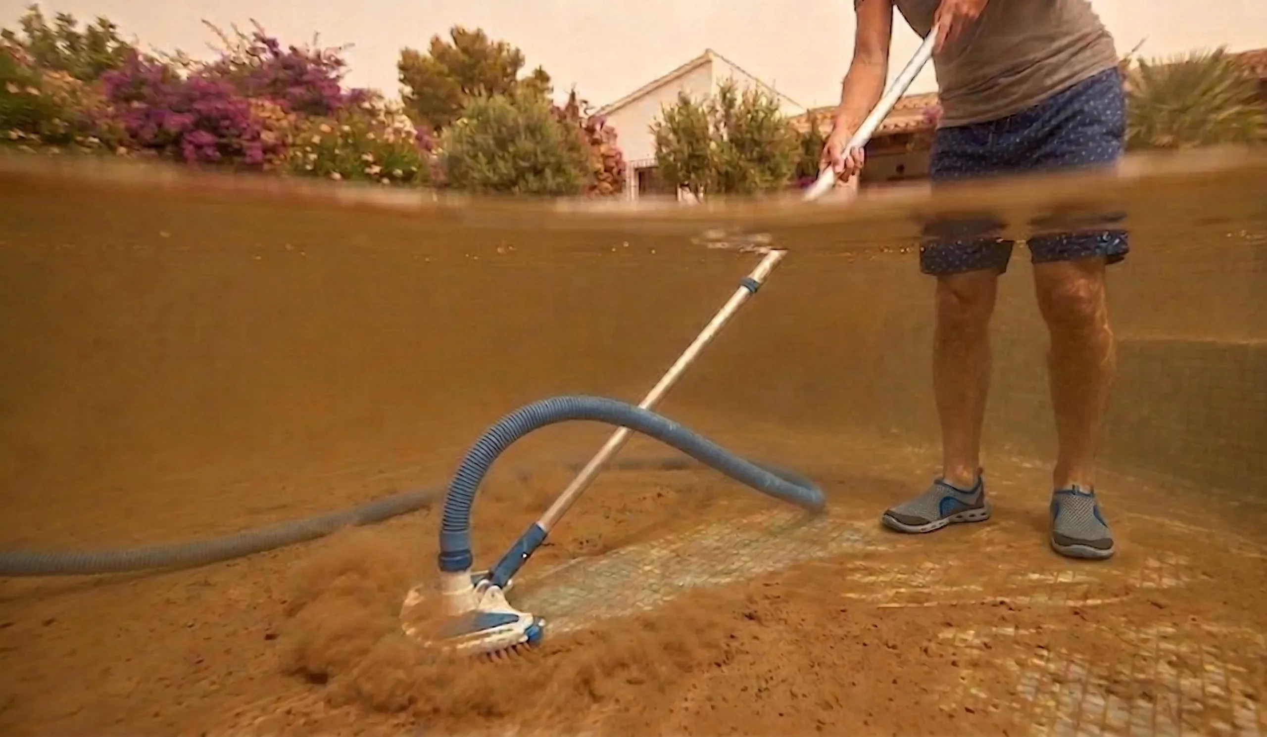 Persona pasando el limpiafondos manual en una piscina con sedimentos de calima.